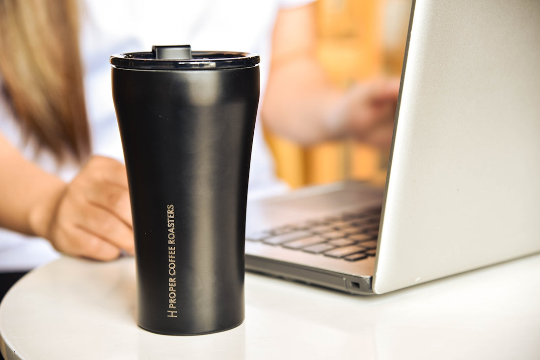 a black coffee cup sitting next to a laptop