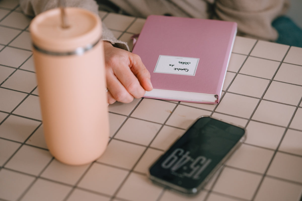 A pink tumbler, book, and phone on a checkered surface.