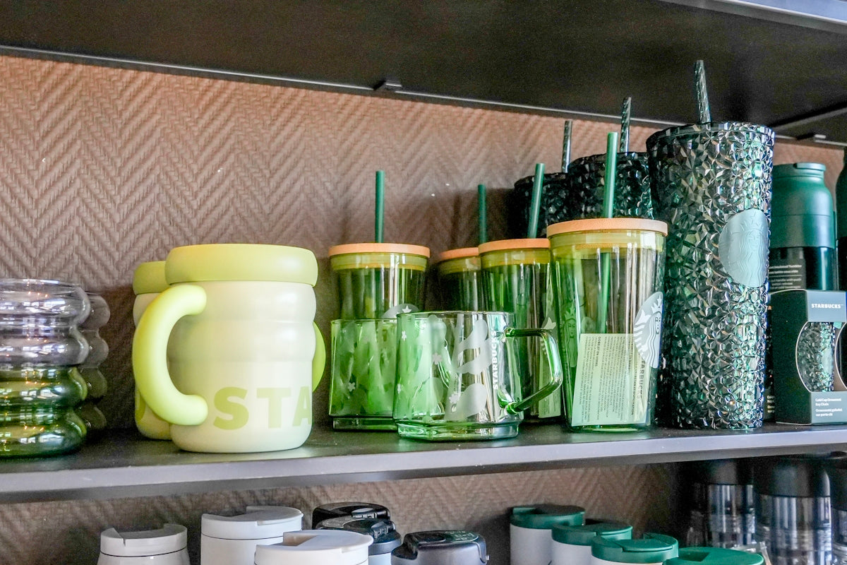 Green and yellow mugs and tumblers displayed on a shelf.